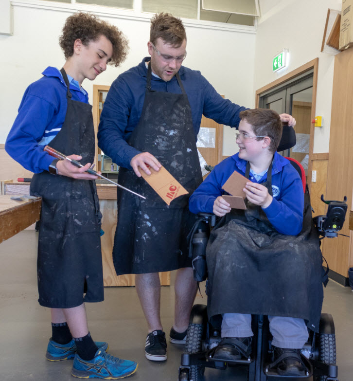 High school woodwork class showing a teacher assisting two students, one of whom is in a wheelchair